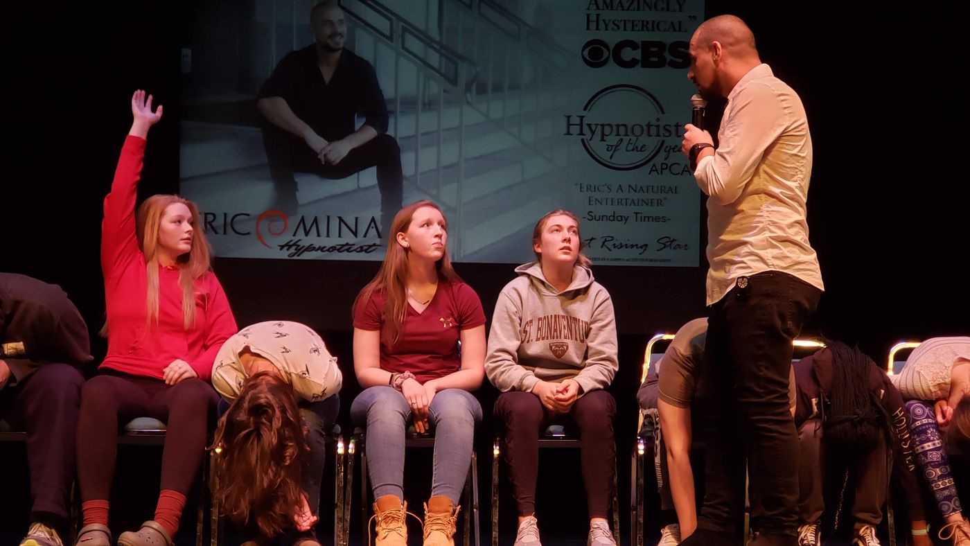 Eric Mina performing hypnosis on stage with student volunteers