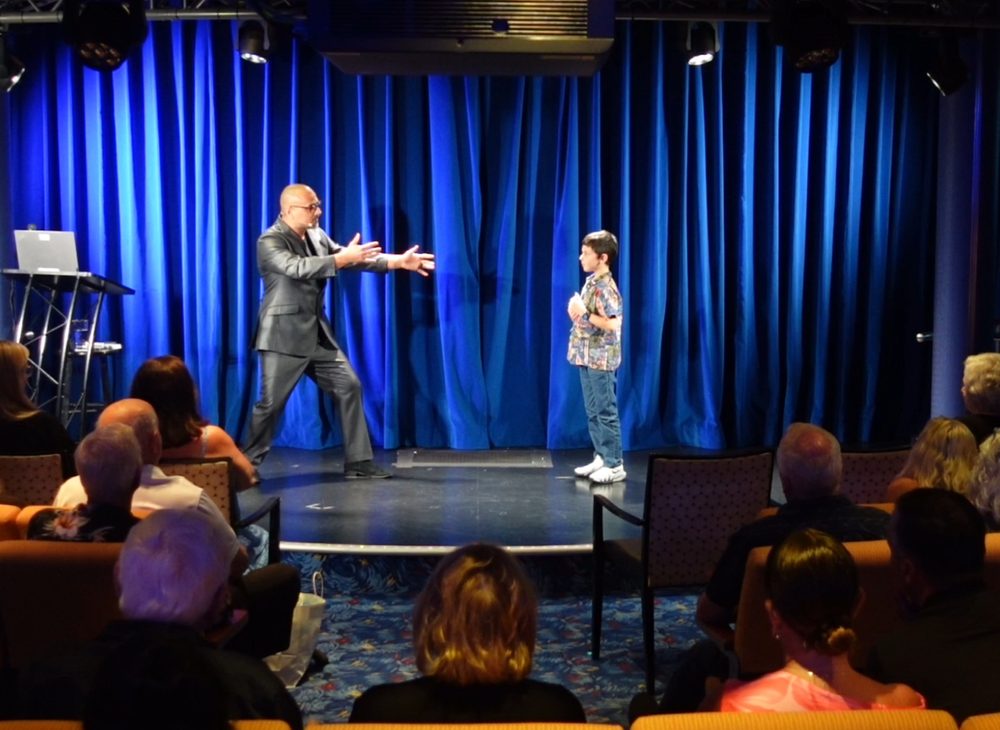 Eric Mina on stage with a volunteer in front of a seated audience